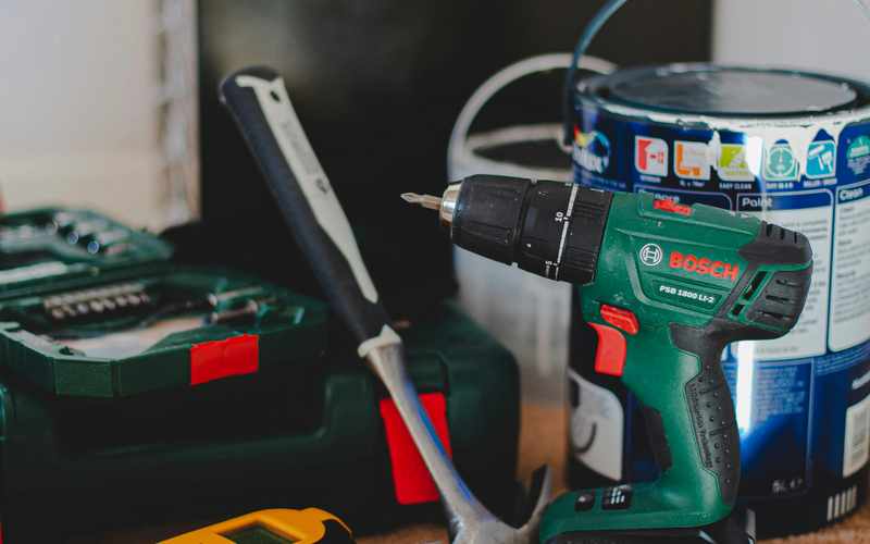 A cordless drill, hammer, and stud finder laid out for a job