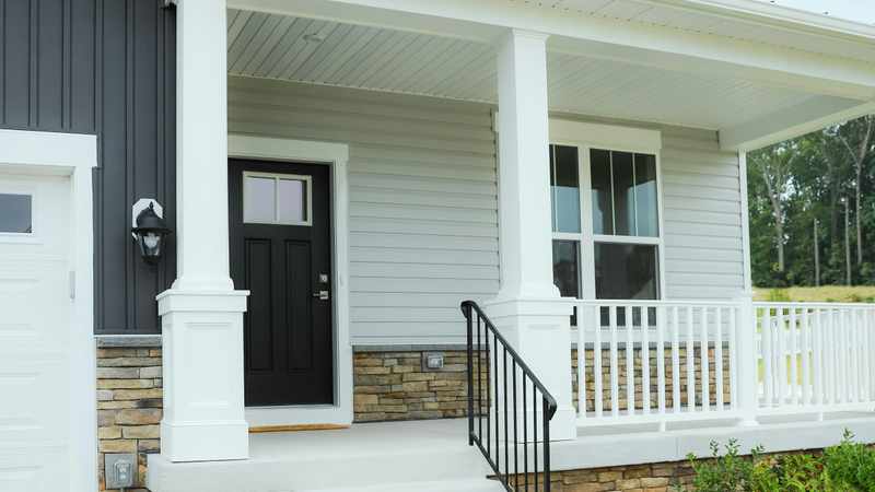 Two-story home exterior with light gray horizontal siding, dark vertical accent siding, and a covered front porch