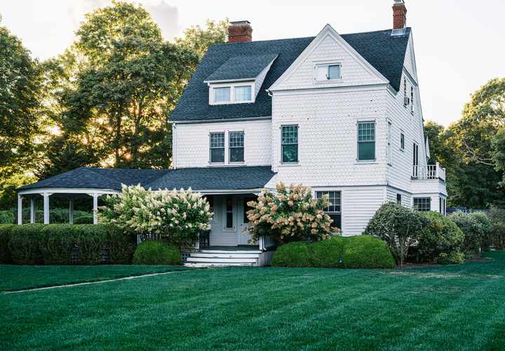 Large white shingle-style two-story home with wraparound porch and mature trees