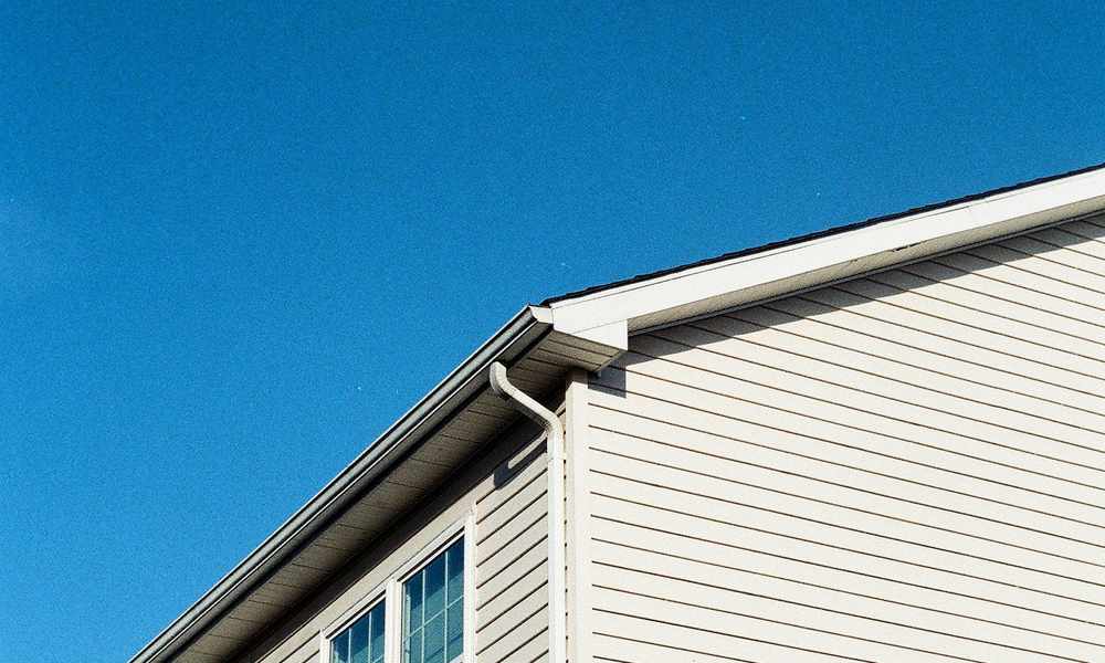 Close-up of a home's lap siding, gutter, and roofline against a clear blue sky