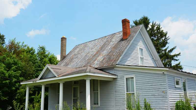 An older home exterior with a weathered metal roof and light-colored wood siding