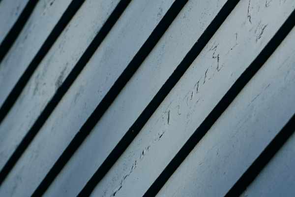 Close-up of diagonal weathered painted board siding with dark shadow gaps between planks