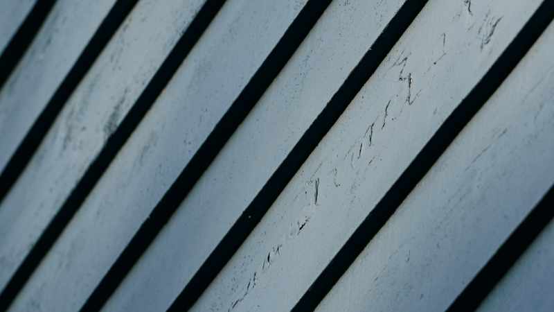 Close-up of diagonal weathered painted board siding with dark shadow gaps between planks