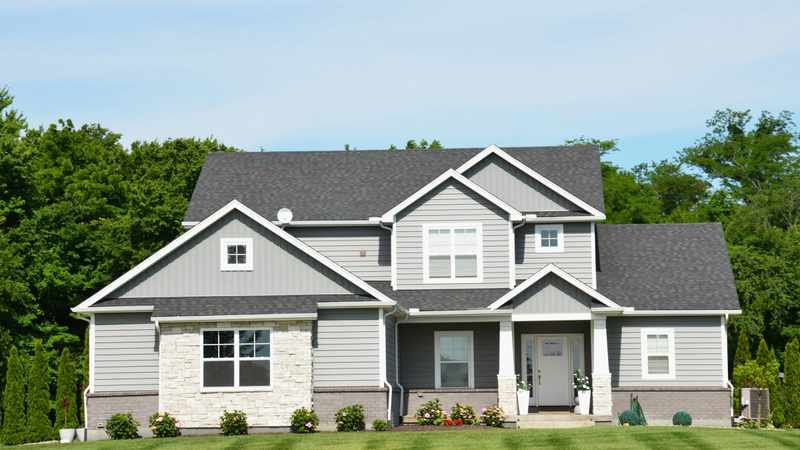 Two-story home exterior with gray vinyl siding, white trim, and stone accents